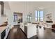 Modern kitchen featuring white cabinets, dark wood floors, island with seating, and access to the living room with expansive windows at 8648 Carneros Ct, Parker, CO 80138
