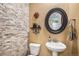 Stylish half bathroom with a decorative stone wall, pedestal sink, and a round decorative mirror at 13326 Olive Way, Thornton, CO 80602