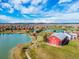Aerial view of a community featuring a red barn, a lake, and green spaces under a cloudy blue sky at 10480 Truckee St # B, Commerce City, CO 80022