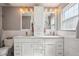 Bright, modern bathroom with double sinks, tile backsplash, white cabinets, brushed hardware, and decorative light fixtures at 5172 S Cody Ct, Littleton, CO 80123