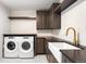 Stylish laundry room featuring modern washer and dryer, brown cabinetry, gold fixtures, and a white farmhouse sink at 754 S York St, Denver, CO 80209