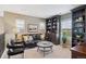 A comfortable living room features a black leather couch, bookshelves, and large windows with plantation shutters at 9528 Pendio Ct, Highlands Ranch, CO 80126