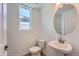 Well-lit half bathroom featuring pedestal sink, round mirror, and neutral color palette at 2916 Oxley St, Strasburg, CO 80136