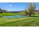 Scenic view of a lush green golf course with a tranquil pond in front of residential buildings and mountain backdrop at 2895 W Riverwalk Cir # 104, Littleton, CO 80123