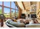 Inviting living room featuring log walls, stone fireplace, and stunning views through large windows at 6150 Bluebell Ln, Evergreen, CO 80439