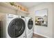 Bright laundry room with white Whirlpool appliances, open shelving, and cool art creating a functional and stylish space at 2153 Flower Blossom Ave, Brighton, CO 80601