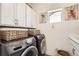 Functional laundry room with modern washer and dryer, ample storage cabinets, and a bright window at 2572 Iola St, Aurora, CO 80010