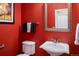 Stylish powder room featuring a pedestal sink, toilet, mirror, and bold red wall color at 13943 W 87Th Ln, Arvada, CO 80005