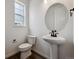 Modern half bathroom featuring a sleek pedestal sink, round mirror, and dark fixtures at 24708 E 40Th Ave, Aurora, CO 80019
