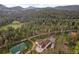 Aerial view of a house, outbuilding, greenhouse, and woods with mountains in the background at 27987 Pine Grove Trl, Conifer, CO 80433