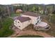 Two-story tan home with a deck, a patio, and a large arched window surrounded by mature trees at 27987 Pine Grove Trl, Conifer, CO 80433