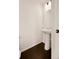A modern half-bathroom featuring a pedestal sink, dark wood floors, and a toilet at 10071 Yampa Ct, Commerce City, CO 80022