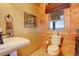 Quaint powder room featuring wood-paneled walls, a pedestal sink, and a window with a pleasant outdoor view at 11450 Marks Dr, Conifer, CO 80433