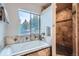 Bathroom with tiled bathtub and shower featuring a window and neutral color palette at 11932 Coal Creek Heights Dr, Golden, CO 80403