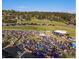 Aerial view of an outdoor community gathering for music with audience, stage, and parked cars on grassy field at 2164 Foothills S Dr, Golden, CO 80401