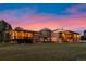 A panoramic exterior showcasing the home's architecture and spacious yard against a vibrant sunset at 11881 County Road 37, Fort Lupton, CO 80621