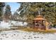 Scenic backyard with a charming wooden gazebo, foot bridge, and mature trees is partially covered in snow at 1333 Mariposa Ave, Boulder, CO 80302