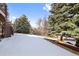 This backyard view features a snowy landscape, mature trees, and a glimpse of the home's deck, inviting outdoor enjoyment at 34 Amaranth Dr, Littleton, CO 80127