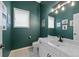 Powder bathroom with green walls, white vanity, framed art and modern lighting at 9 Mule Deer Trl, Littleton, CO 80127