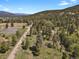 An aerial view shows the property set among lush greenery with trees and rolling hills at 9359 Barnes Ave, Conifer, CO 80433