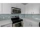 Close-up of sleek stainless steel appliances complemented by white cabinets and stone countertops; tiled backsplash adds to appeal at 13456 Via Varra # 401, Broomfield, CO 80020