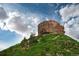 Scenic view of Castle Rock landmark against a backdrop of green hills and a partly cloudy blue sky at 777 Whispering Oak Dr, Castle Rock, CO 80104