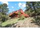 Exterior view of a rustic home with a sprawling wrap-around deck on a sloped lot surrounded by trees at 1278 Aspen Dr, Evergreen, CO 80439