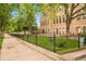 Exterior view of a converted brick schoolhouse with mature landscaping and a wrought iron fence at 1140 Columbine St # 106, Denver, CO 80206