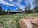 Charming single-story home with brown siding, green roof, deck, and large boulders in the foreground at 11608 Apache Trl, Conifer, CO 80433