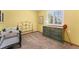 Bedroom with yellow walls, large window, and a variety of furniture including a crib and an antique dresser at 4390 S Sheridan Blvd, Littleton, CO 80123