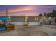 Charming single-story home featuring a concrete yard, covered parking, and a warm, inviting exterior under a colorful evening sky at 481 Cragmore St, Denver, CO 80221
