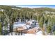 Aerial view of a gray mountain home nestled among tall pine trees with a snow-covered landscape and blue sky at 10747 Timothys Dr, Conifer, CO 80433