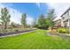 Expansive backyard featuring lush green lawn, stone retaining wall, mature trees, and a charming wooden deck for outdoor entertaining at 5686 Brook Hollow Dr, Broomfield, CO 80020