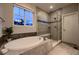 Modern bathroom with a soaking tub, glass-enclosed shower, tile surround, and bright natural light from the window at 6652 W Asbury Pl, Lakewood, CO 80227
