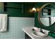 Bathroom with green walls, white and blue tile, round mirror, and black vanity at 7039 Otis Ct, Arvada, CO 80003