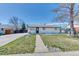 Inviting single-story house with a lush green lawn, mature tree, and a classic white brick facade at 7621 Granada Rd, Denver, CO 80221