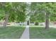Charming home with mature trees, green lawn, and a concrete walkway leading to the front door at 2812 Krameria St, Denver, CO 80207