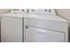 A side-by-side, white, top-load washer and dryer combo sits against a neutral colored wall at 1417 Bloom St, Brighton, CO 80601