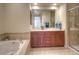 Bright bathroom featuring a double vanity, soaking tub, and glass-enclosed shower stall, all with tile accents at 8594 W Quarto Ave, Littleton, CO 80128