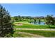 Scenic golf course view featuring lush green fairways, mature trees, a pond, and nearby residential buildings under a clear blue sky at 7882 Vallagio Ln, Englewood, CO 80112