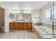 Bright bathroom with double sinks, wooden cabinets, a large soaking tub, and tile flooring at 12702 E 105Th Ave, Commerce City, CO 80022