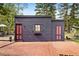 Unique building with a dark wood exterior, red doors, a brick patio, and surrounding foliage, creating rustic charm at 715 Main St, Georgetown, CO 80444
