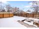 Snowy backyard with a wooden fence, patio area, and mature trees, ideal for outdoor enjoyment at 2647 N High St, Denver, CO 80205