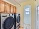 Modern laundry room with front-load washer and dryer, wood cabinets, and access to an adjacent room at 1674 Bent Grass Cir, Castle Rock, CO 80109