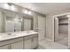Bright bathroom featuring a double sink vanity, large mirror, and glass enclosed shower and access to walk-in closet at 13486 Valentia St, Thornton, CO 80602