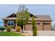 The home features a two-car garage, manicured lawn, mature trees, and exterior stone details at 10653 E 163Rd Ct, Brighton, CO 80602