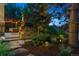 Landscaped backyard with stone fireplace, outdoor seating, and a stone pathway through lush plants at 35 Brookhaven Pl, Littleton, CO 80123