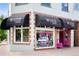 Corner storefront featuring black awnings and vibrant pink door, advertising 