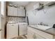 Bright laundry room with washer, dryer, sink, gray cabinets and patterned wallpaper at 8444 E 55Th Pl, Denver, CO 80238