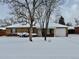 Ranch style home with brick exterior, snowy lawn, and attached garage at 1244 Racine St, Aurora, CO 80011